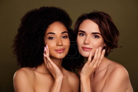 Téléchargez les photos : Portrait de deux jeunes femmes étonnantes toucher joue esthétique pure application lotion isolée sur fond de couleur kaki. - en image libre de droit