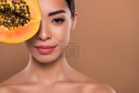 Téléchargez les photos : Portrait de magnifique jeune fille seins nus couvrant oeil doux papaye fruit masque facial isolé sur fond de couleur beige. - en image libre de droit