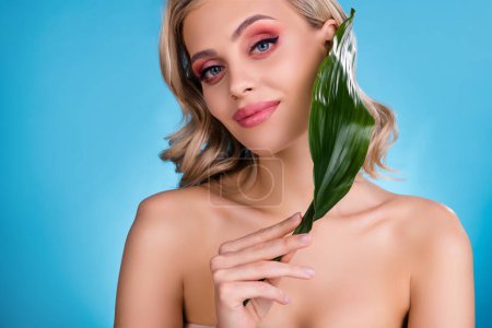 Téléchargez les photos : Photo de dame chic féminine modèle riche en utilisant la crème biologique avec extrait de fleur de plante verte sur fond bleu. - en image libre de droit