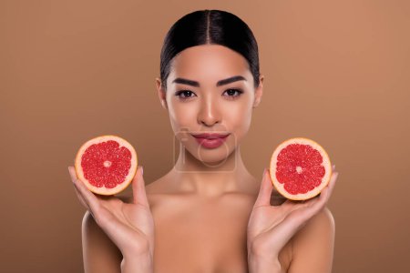 Foto de Concepto de niña foto sosteniendo rodajas de pomelo maduras para hidratación de la piel aislada sobre fondo de color beige. - Imagen libre de derechos