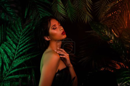 Photo for Photo of chinese vietnamese girl over dark exotic palm tree leaves touch hands shoulder with closed eyes. - Royalty Free Image