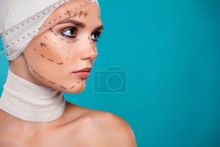 Téléchargez les photos : Photo de dame utilisant règle pour la chirurgie plastique changement asymétrie faciale isolé sur fond de couleur cyan. - en image libre de droit