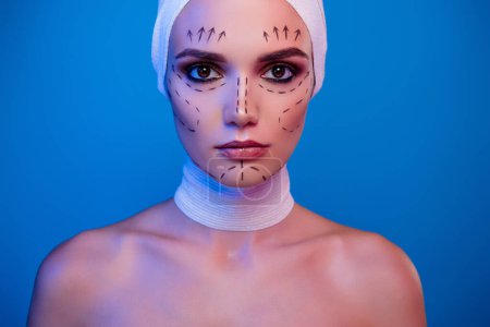 Foto de Foto de chica atractiva paciente de cirugía plástica que tiene marcas de corrección de dibujo en la cara mirar sobre el fondo de neón. - Imagen libre de derechos
