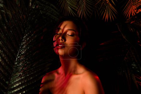 Photo for Photo of vietnamese asian girl closing eyes surround by dark tropical plants. - Royalty Free Image