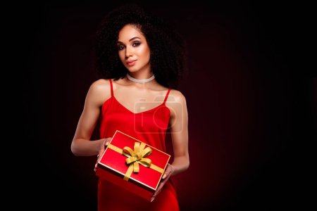 Téléchargez les photos : Photo de superbe dame élégante tentante présentant boîte cadeau isolé sur fond de couleur rouge foncé. - en image libre de droit