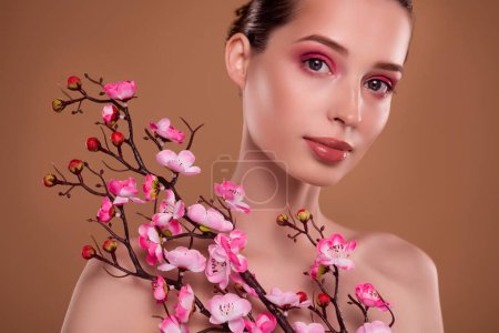 Foto de Foto de la señora atractiva bastante impresionante que sostiene la loción del cuerpo de la rama de la flor rosada para la piel ideal sobre fondo pastel. - Imagen libre de derechos