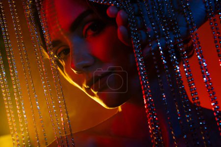 Photo for Photo of adorable sweet woman naked shoulders standing behind rhinestones chains isolated red neon color background. - Royalty Free Image