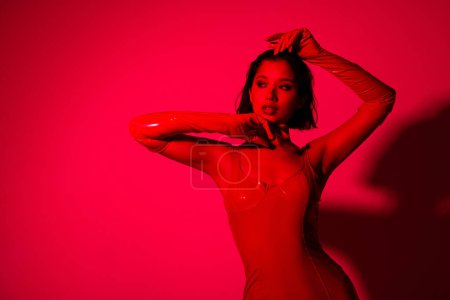 Foto de Foto de impresionante joven sexy mirada espacio vacío vestido ropa de cuero rojo aislado sobre fondo de luz de neón rojo. - Imagen libre de derechos