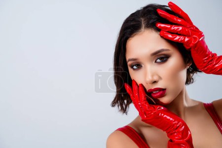 Foto de Foto de mujer joven atractiva mirada cara táctil cámara vestida ropa de cuero rojo aislado sobre fondo gris claro. - Imagen libre de derechos