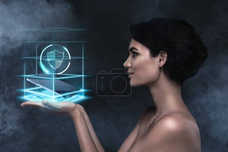 Téléchargez les photos : Collage futuriste créatif de femme tenir la main démontrer téléphone protégé de haute qualité avec le programme de bouclier holographique. - en image libre de droit