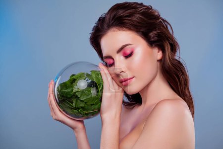 Téléchargez les photos : Photo de femme tenir la sphère de verre vert plante toucher joues fermer les yeux isolé gris couleur arrière-plan. - en image libre de droit