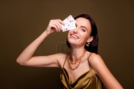 Photo for Photo of cheerful stunning woman in khaki silky dress cover eye with cards ace isolated on brown color background. - Royalty Free Image