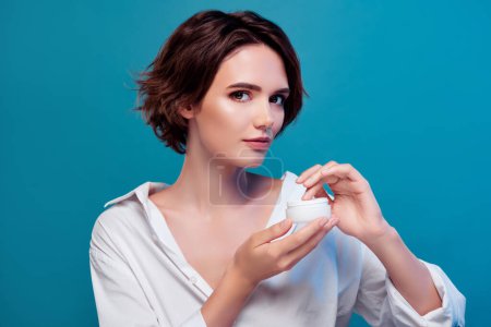 Photo for Portrait of stunning gentle lady apply cream on facial soft silky skin using lotion isolated on blue color background. - Royalty Free Image