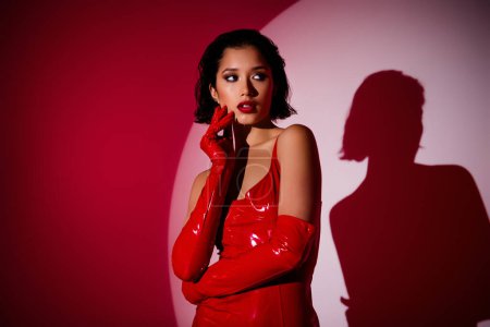 Foto de Foto de hermosa chica joven mirada sexy espacio vacío vestido ropa de cuero rojo aislado sobre fondo de luz de neón rojo. - Imagen libre de derechos