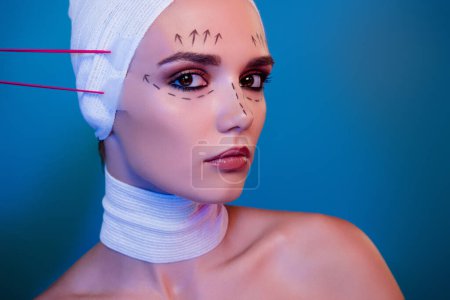 Foto de Foto de chica atractiva en vendaje médico que tiene procedimiento facial de elevación de cinta sobre fondo de color azul. - Imagen libre de derechos