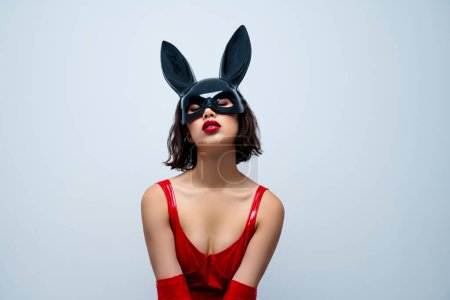 Téléchargez les photos : Photo de superbe dame montrer poitrine fermé yeux lapin masque rouge vêtement en cuir isolé sur fond gris clair. - en image libre de droit