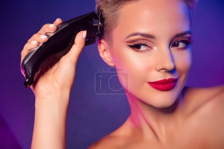 Téléchargez les photos : Photo de fille avec relooking lumineux en utilisant tondeuse à cheveux pour faire coiffure pixie sur fond de couleur vive. - en image libre de droit