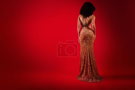 Photo for Photo of stunning fancy woman with bare back and slim sexy figure in sparkling dress on dark red color background. - Royalty Free Image
