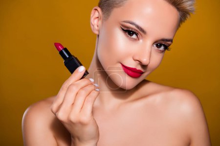 Téléchargez les photos : Photo de femme tenir rouge à lèvres pommade isolé jaune fond de couleur moutarde. - en image libre de droit