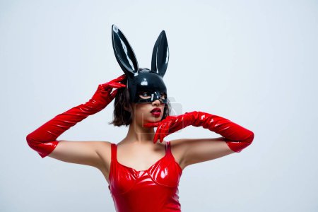 Foto de chica hermosa cara táctil mirada espacio vacío conejo máscara traje de cuero rojo aislado sobre fondo gris claro.