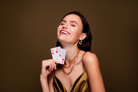 Téléchargez les photos : Photo de gaie femme élégante tenant des cartes as full house et jeu gagnant isolé sur fond de couleur marron. - en image libre de droit
