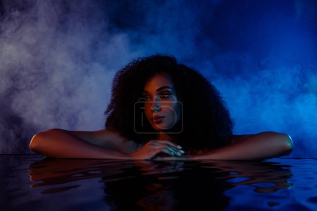 Téléchargez les photos : Portrait de dame nue nageant dans la piscine au centre de villégiature spa luxueux éclairé sombre lumière. - en image libre de droit