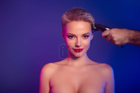 Foto de Foto de chica con maquillaje brillante tienen procedimiento peluquería corte de pelo a mano con trimmer. - Imagen libre de derechos