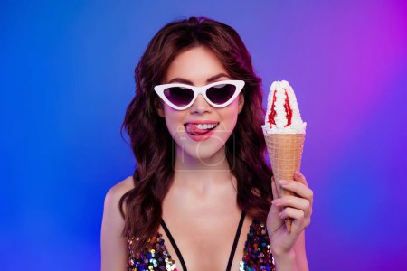Foto de Foto retrato de mujer joven atractiva lamer dientes mantenga sabroso helado aislado sobre fondo de neón retro luz. - Imagen libre de derechos