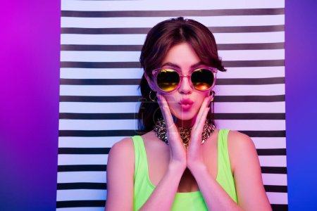 Photo for Photo of cool girl in sunglass touch hands cheeks make pouted lips send air kiss over striped board neon background. - Royalty Free Image