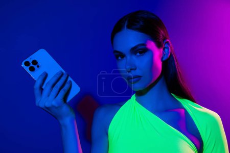 Téléchargez les photos : Portrait de séduisant fantaisie modèle fille main tenir téléphone intelligent isolé sur fond de lumière au néon couleur pourpre. - en image libre de droit