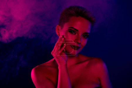 Téléchargez les photos : Photo de dame aux yeux fumés relooking toucher les mains visage sur néon lumineux fond brumeux. - en image libre de droit