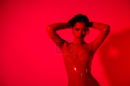 Foto de Foto de impresionante joven dama tacto pelo sexy pose caliente desgaste prenda de cuero rojo aislado sobre fondo de luz de neón rojo. - Imagen libre de derechos