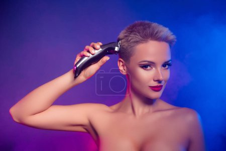 Téléchargez les photos : Photo de femme utilisant une tondeuse à cheveux pour faire une coiffure isolée sur fond dégradé de couleur vive. - en image libre de droit