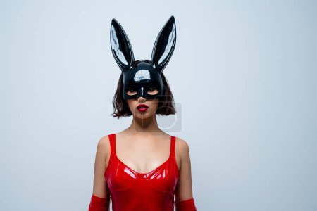 Foto de Foto de hermosa chica sex shop banner promocional conejo máscara traje de cuero rojo aislado sobre fondo gris claro. - Imagen libre de derechos