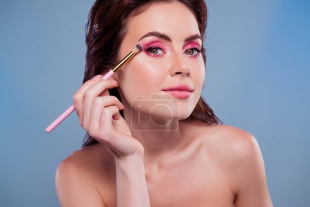 Foto de Foto de cerca de la mirada de la mujer usando cepillo para las sombras de los ojos fondo de color gris aislado. - Imagen libre de derechos