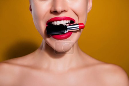 Foto de Foto recortada de mordedura de mujer mantenga el brillo de los labios rojos aislados sobre el fondo de color amarillo mostaza. - Imagen libre de derechos