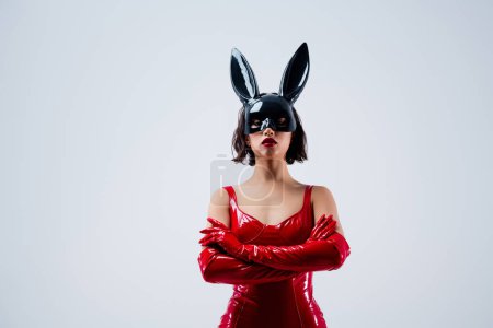 Téléchargez les photos : Photo de magnifique fille mains pliées pose confiante masque de lapin tenue en cuir rouge isolé sur fond gris clair. - en image libre de droit