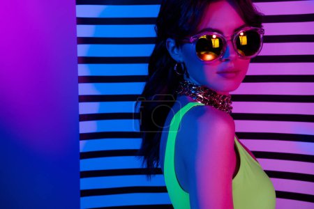 Photo for Photo of cool girl in sunglass stand profile side look camera over striped wall neon ultraviolet background. - Royalty Free Image