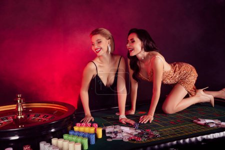 Photo for Photo of two charming laughing ladies wear sexy dresses enjoying playing roulette isolated red fog background. - Royalty Free Image