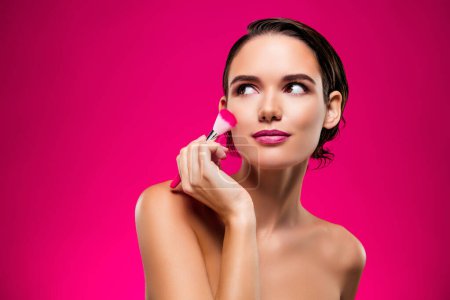 Foto de Foto retrato de mujer joven atractiva aplicar la cara cepillo espacio vacío hombros aislados sobre fondo de color rosa. - Imagen libre de derechos