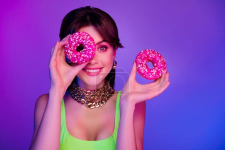 Foto de Photo of happy girl hide eye with delicious cookie with sprinkles isolated multicolor neon background. - Imagen libre de derechos