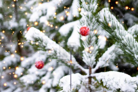 Foto de El fuego de Bengala arde en el bosque de invierno sobre el fondo de los árboles de Navidad decorados con bolas rojas. Árbol de Navidad. El ambiente de Navidad y Año Nuevo. - Imagen libre de derechos