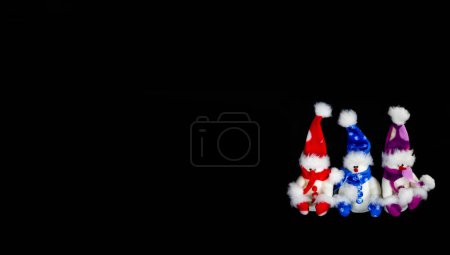 Foto de Banner con tres muñecos de nieve de juguete hechos a mano con sombreros y bufandas sobre un fondo negro. Concepto de Navidad y Año Nuevo. - Imagen libre de derechos