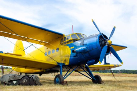 Nahaufnahme eines kleinen gelb-blauen Flugzeugs, das auf einem Feld steht. Alte Propellerflugzeuge in Nahaufnahme.