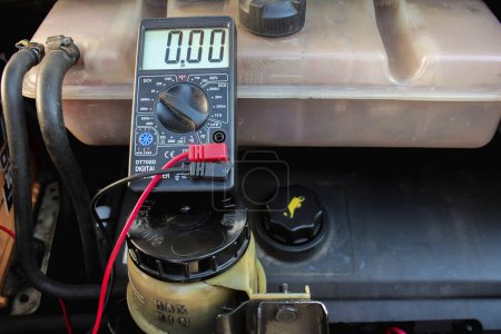 Checking voltage with multimeter. Recovery of acid batteries, resuscitate car battery. Voltmeter to check voltage level on car battery. Car service station. Car repair.
