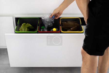 Ein kleines Kind sortiert in der Küche in Zeitlupe Müll in Containern. Moderne Küche mit einem System zur Mülltrennung. Mülltrennkonzept. Keine Verschwendung. Umweltfreundlich.