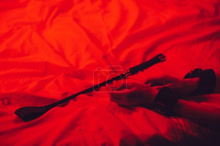 Photo for Girl hands in handcuffs and leather whip flogger for BDSM sex with submission and domination lie on bed in bedroom - Royalty Free Image