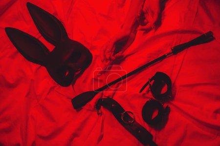 Téléchargez les photos : Set of BDSM accessories with female hands is lying on bed. Flogger whip, handcuffs, mask and choker for sex with submission and domination - en image libre de droit