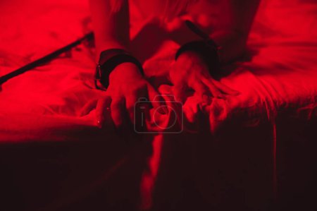 Foto de Girl hands in handcuffs and leather whip flogger for BDSM sex with submission and domination lie on bed in bedroom - Imagen libre de derechos