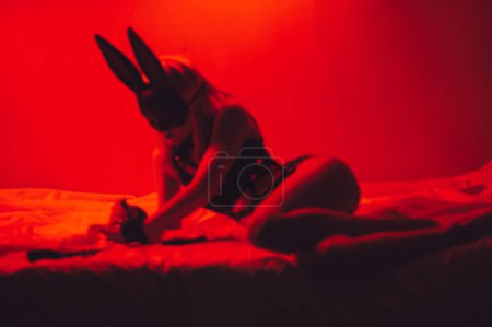 Téléchargez les photos : Blurry silhouette of sexy submissive girl in underwear and a mask lies on bed in bedroom. BDSM concept of sex with submission and domination - en image libre de droit